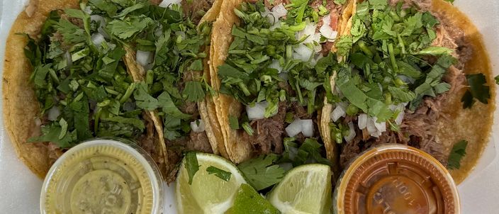 Three small tacos on doubled corn tortillas topped with chopped onion and coriander, with lime wedges and two salsa cups