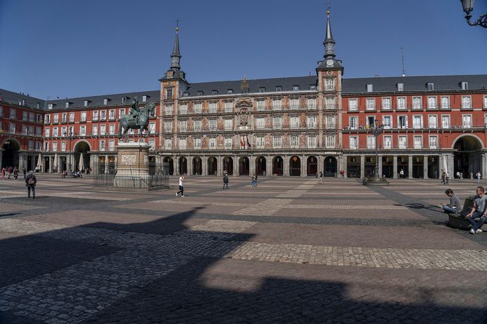 Plaza Mayor's arcaded red-brick facade with twin spires and the bronze equestrian statue of Philip III on the wide paved square under a clear blue sky