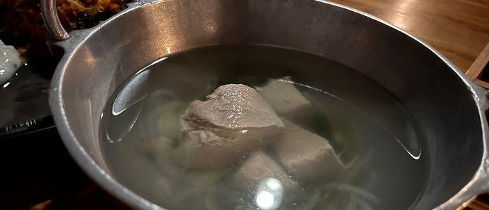 A metal pot of garudhiya — clear tuna broth with chunks of poached fish — served alongside rice on the side.