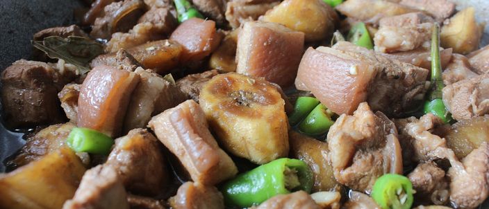A pan of Filipino pork adobo, the meat braised dark and glossy in a reduced vinegar-and-soy sauce with whole green chillies.
