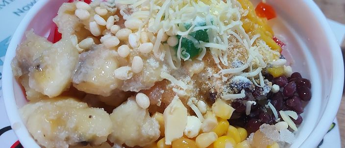 A bowl of halo-halo: shaved ice loaded with sweet corn, red mung beans, strips of yellow jackfruit and a scatter of toasted pinipig rice flakes.
