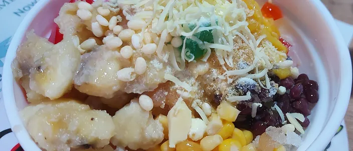 A bowl of halo-halo: shaved ice loaded with sweet corn, red mung beans, strips of yellow jackfruit and a scatter of toasted pinipig rice flakes.