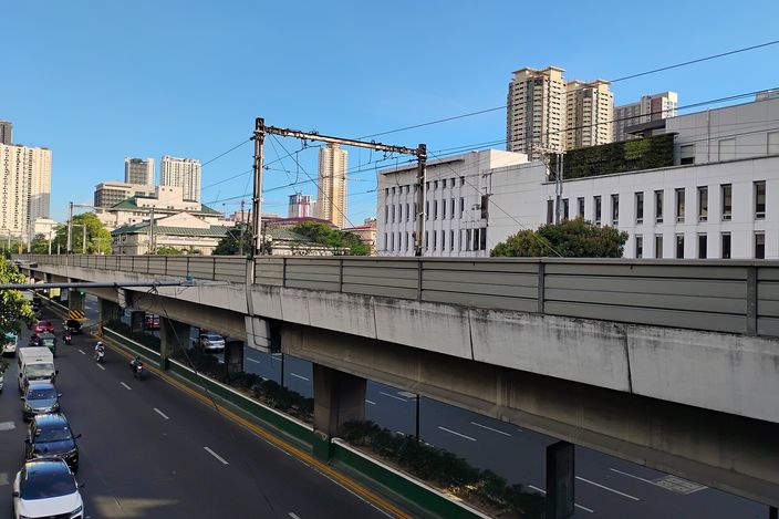 An elevated LRT-1 concrete viaduct with overhead catenary wires running above Taft Avenue in Ermita, cars queuing on the road below under a clear blue sky with mid-rise towers behind.