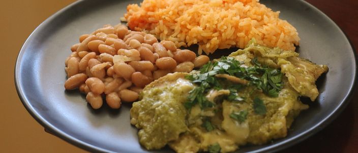 A plate of green chilaquiles — fried tortilla simmered in tomatillo salsa, topped with crema, crumbled white cheese, onion and coriander — served with Mexican rice and refried beans.