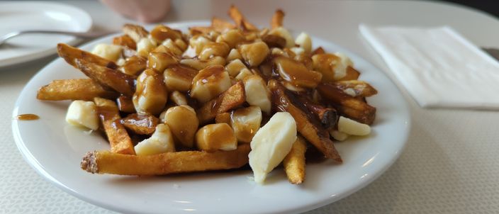 A plate of classic poutine: golden chips topped with distinct white cheese curds and brown gravy poured over, the curds sitting in separate lumps rather than melted flat.