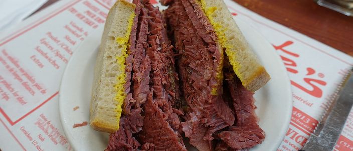 A Montréal smoked meat sandwich cut in half on a plate, showing hand-cut cured beef piled high between two slices of yellow-mustarded rye bread.