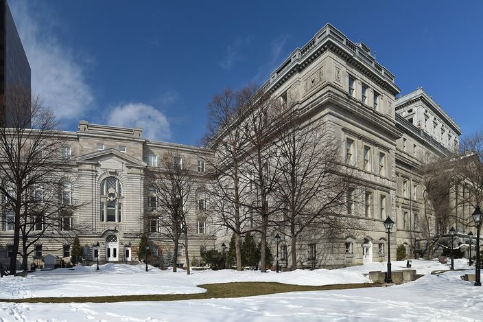 The grey-stone Second Empire Lucien-Saulnier building (old courthouse) in Vieux-Montréal under a clear blue winter sky, with bare trees and patches of snow on the lawn in front.