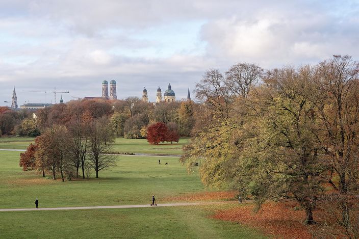 View across the Englischer Garten's autumn lawns and trees from the Monopteros, with the twin domes of the Frauenkirche and the Theatinerkirche on the Old Town skyline beyond