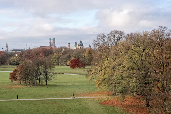 View across the Englischer Garten's autumn lawns and trees from the Monopteros, with the twin domes of the Frauenkirche and the Theatinerkirche on the Old Town skyline beyond