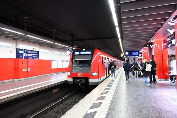 A red-and-white S-Bahn train (S8, destination Herrsching) standing at an underground platform of München Hauptbahnhof, with passengers boarding on the right and the platform sign reading 'Hauptbahnhof'.