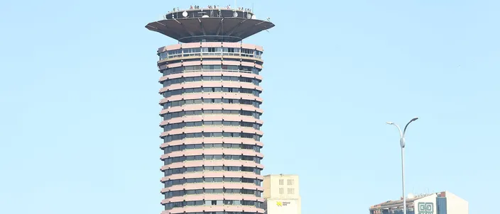 A round twenty-eight-story concrete tower ribbed with balconies, topped by a wide saucer-shaped viewing deck with figures standing on its rim, against a clear pale blue sky.