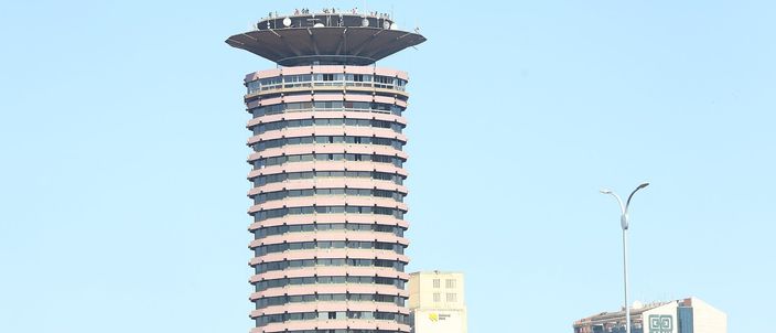 A round twenty-eight-storey concrete tower ribbed with balconies, topped by a wide saucer-shaped viewing deck with figures standing on its rim, against a clear pale blue sky.