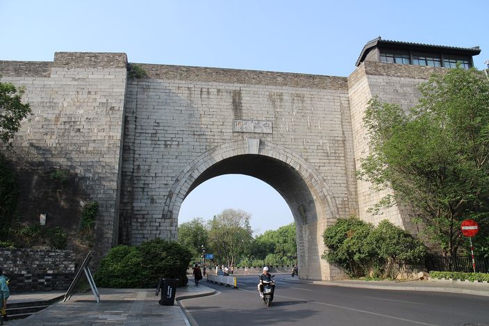 Zhonghua Gate's fortress-like stone arch and crenellated tower, seen from the street below under a clear sky.