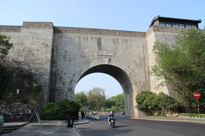 Zhonghua Gate's fortress-like stone arch and crenellated tower, seen from the street below under a clear sky.