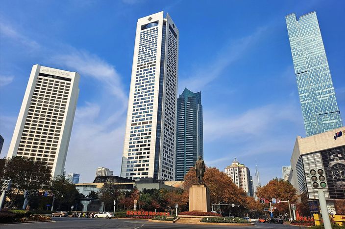 Xinjiekou roundabout in central Nanjing on a clear day: the Sun Yat-sen statue at street level with a cluster of glass-and-steel office towers and hotels rising behind it.