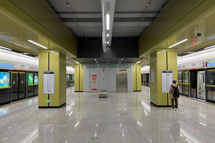 An empty, brightly lit Nanjing Metro platform at Shiyanglu station, ochre-tiled columns on either side and a train waiting with its doors open.