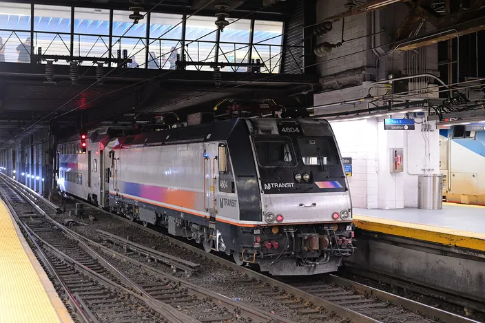 A silver and blue New Jersey Transit locomotive at rest beside a platform in the low-ceilinged, artificially lit trainshed of New York Penn Station.
