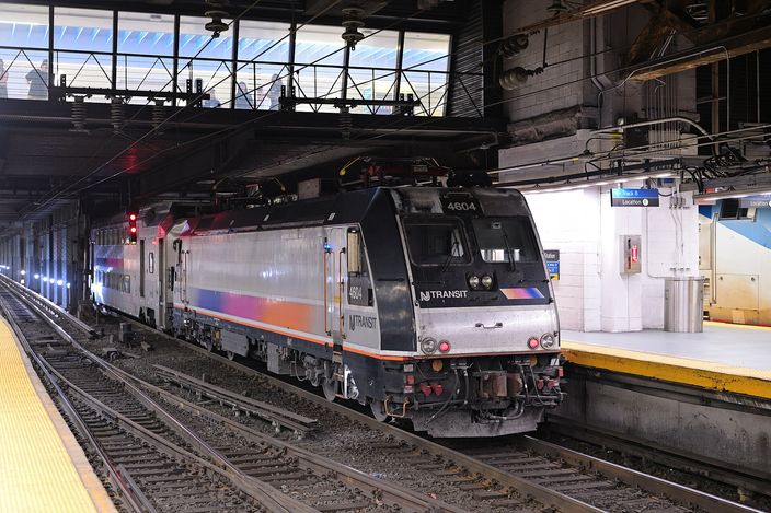 A silver and blue New Jersey Transit locomotive at rest beside a platform in the low-ceilinged, artificially lit trainshed of New York Penn Station.