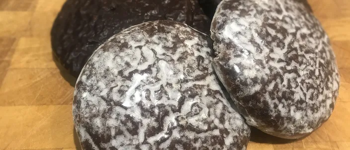 Three round, dark Lebkuchen with a thin crackled white sugar glaze, piled on a wooden board
