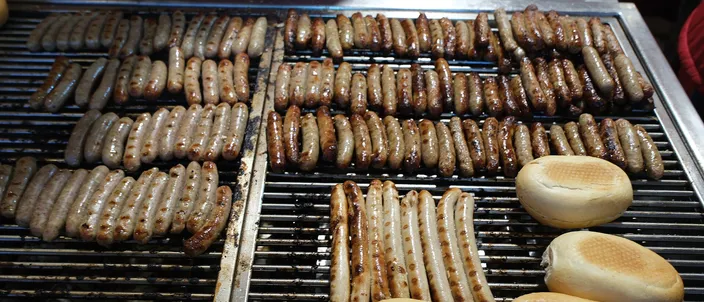 Rows of small, finger-sized grilled bratwurst browning on a market grill beside split bread rolls, at Nuremberg's Christmas market