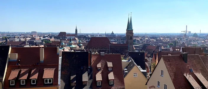 The red-tiled roofs of Nuremberg's old town seen from the castle hill, the twin green spires of St. Sebald's church rising on the right under a clear blue sky