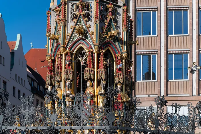 The gilded and painted Gothic spire of the Schöner Brunnen fountain behind its wrought-iron railing on Nuremberg's main market square