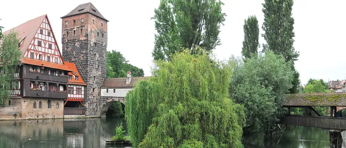 The half-timbered Weinstadel and the stone water tower beside the covered wooden Henkersteg bridge, reflected in the river Pegnitz among willows