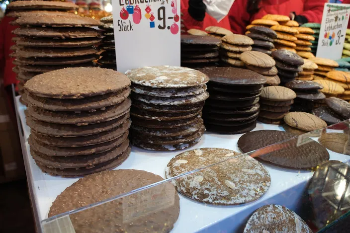 Stacks of round Lebkuchen on a market counter, plain, glazed and studded with almonds, a handwritten price card behind them