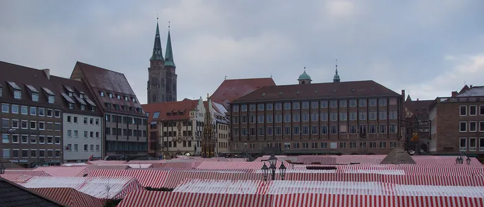 The Christkindlesmarkt on Nuremberg's Hauptmarkt seen from above: a sea of red-and-white striped cloth roofs, the gilded spire of the Schöner Brunnen among them and the two towers of St. Sebald beyond the square's buildings