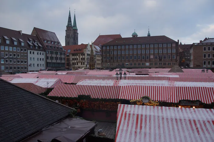 The Christkindlesmarkt on Nuremberg's Hauptmarkt seen from above: a sea of red-and-white striped cloth roofs, the gilded spire of the Schöner Brunnen among them and the two towers of St. Sebald beyond the square's buildings