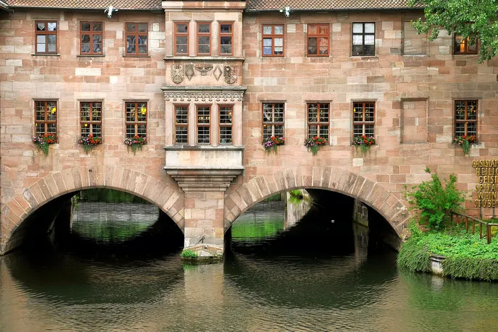 The sandstone Heilig-Geist-Spital standing on two arches over the river Pegnitz, flower boxes in its windows and green water below