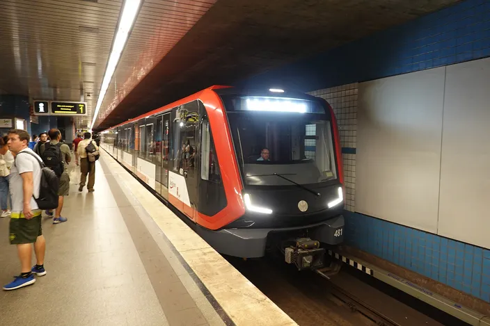 A new red-and-silver U-Bahn train with its lights on pulling into an underground platform in Nuremberg, passengers waiting