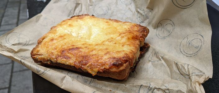 A croque-monsieur on its paper wrapper, the béchamel top blistered and browned