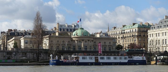 The Seine seen from the Right Bank quai, a moored tour boat along the far embankment and the domed Musée de la Légion d'honneur rising behind it, bare trees and a bright cloudy sky