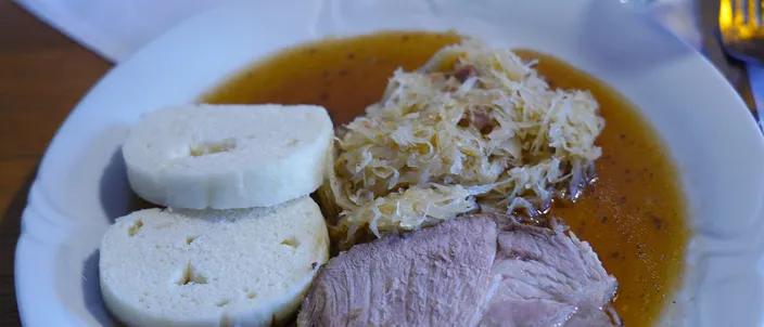 A plate of vepřo knedlo zelo: two slices of roast pork with gravy, two discs of white bread dumpling, and a mound of braised sauerkraut