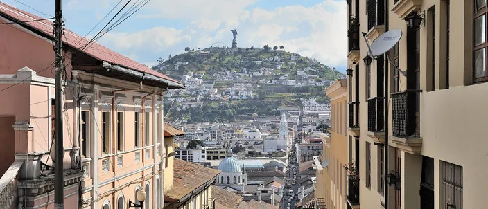 Calle García Moreno running steeply downhill between colonial houses with balconies, toward the domes of the old town and the green hill of El Panecillo crowned by its winged Virgin statue