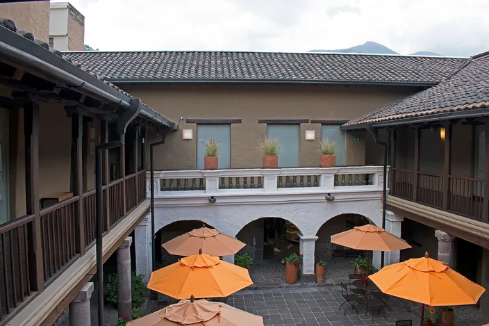 The inner courtyard of the Casa del Alabado, a restored colonial house with wooden galleries, a tiled roof and orange umbrellas over the patio
