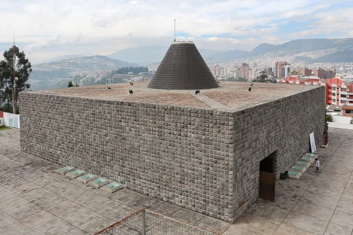 La Capilla del Hombre in Quito: a square building of grey stone blocks with a dark conical dome, on a terrace above the northern city and the hills