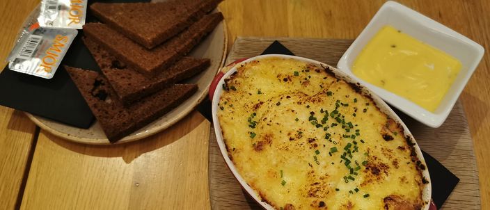 A dish of browned plokkfiskur with chives beside slices of dark rye bread and a pot of butter