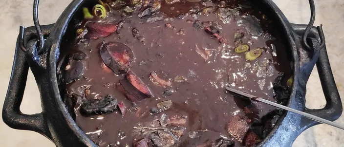 A close-up of feijoada in a pot: a dark stew of black beans with slices of sausage and pieces of pork.