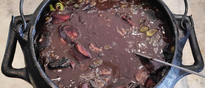 A close-up of feijoada in a pot: a dark stew of black beans with slices of sausage and pieces of pork.