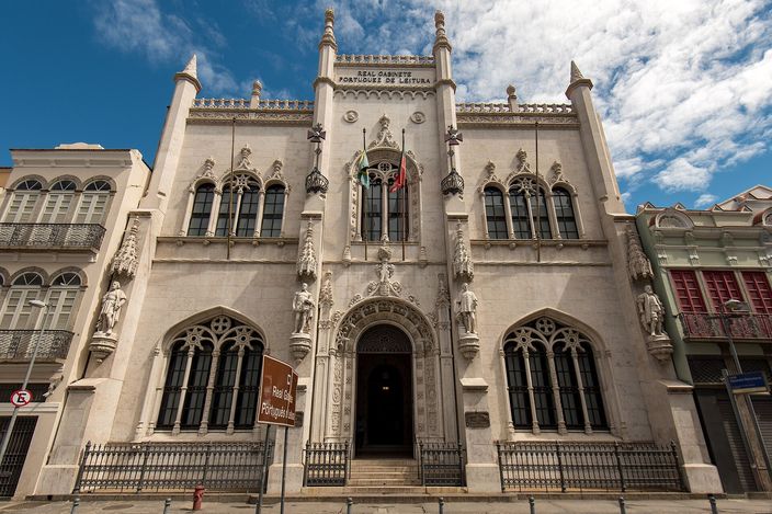 The carved pale limestone front of a neo-Manueline library, with pinnacles, four statues in niches and a pointed arched doorway, under a blue sky