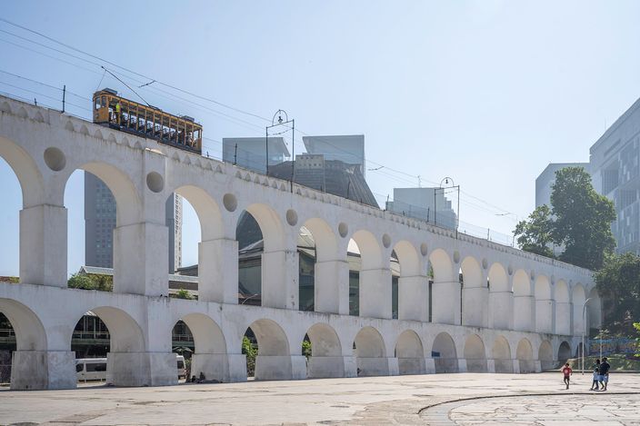 The yellow bondinho tram crossing the tall white Arcos da Lapa aqueduct arches, with modern towers of Centro behind under a clear sky