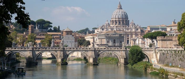 The Tiber flowing under Ponte Sant'Angelo with St Peter's Basilica dome rising above the west bank rooftops in daylight