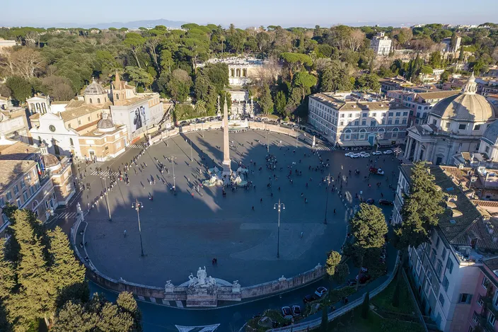 Piazza del Popolo from above in winter sun: the full oval of the square with its Egyptian obelisk at the center, the twin domed churches at the mouth of the streets fanning south, the wooded Pincian terrace and its fountain rising along one side.
