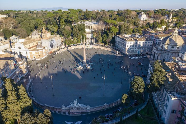 Piazza del Popolo from above in winter sun: the full oval of the square with its Egyptian obelisk at the centre, the twin domed churches at the mouth of the streets fanning south, the wooded Pincian terrace and its fountain rising along one side.