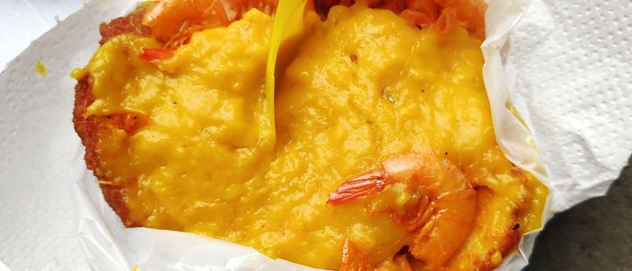 An acarajé split open on white paper at a stall, the fried black-eyed-pea fritter filled with orange vatapá and dried prawns.