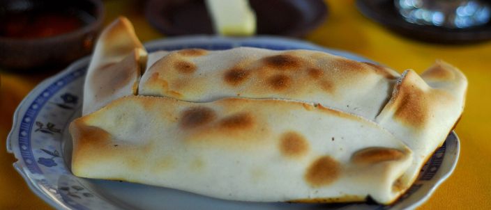 A single large baked empanada de pino on a plate: a plump golden pastry folded into a rectangle with a crimped edge, a small dish of salsa behind it.