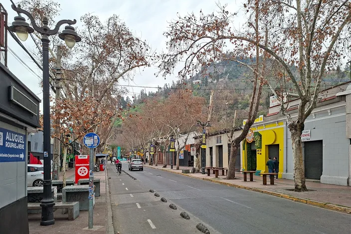 Calle Pío Nono in Bellavista: a low-rise commercial street lined with plane trees losing their leaves, cafés and bars behind, with the wooded slope of Cerro San Cristóbal rising at the far end