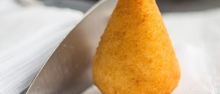 A single golden, crisp teardrop-shaped coxinha resting on a white napkin, narrowing to a rounded point at the top.